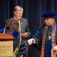 Provost Cimitile on stage with President Emeritus Haas and shaking hands with a  faculty member.